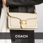 Beige Coach handbag with a gold clasp, worn over a black coat, showcasing a stylish and elegant accessory for modern fashion.